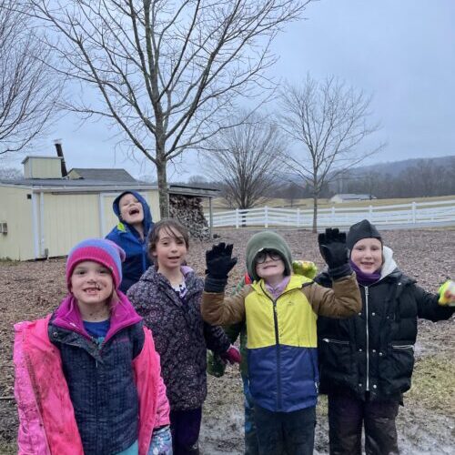 Five children pose outside in the rain, smiling at the camera