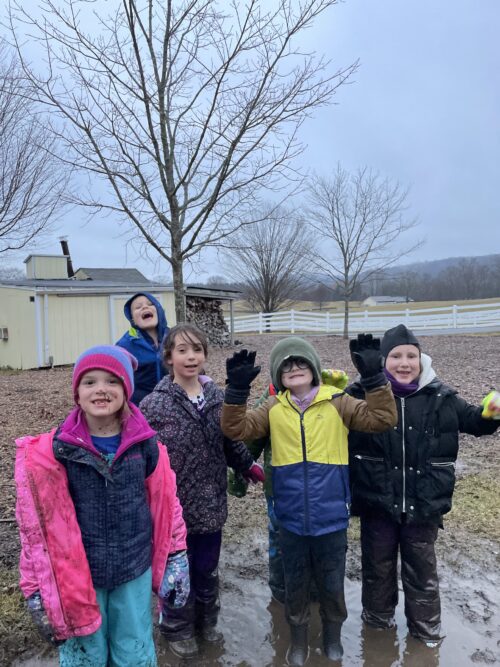 Five children pose outside in the rain, smiling at the camera